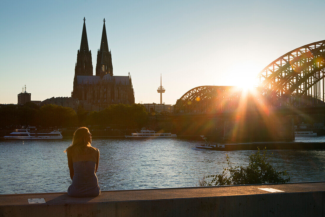 Young woman sitting on the Rhine river banks opposite to the cathedral, Cologne, North Rhine-Westphalia, Germany, Europe