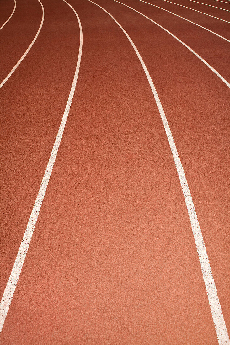 The surface of a sports ahtletics running track in Thousand Oaks, California, USA. Red surface with white painted lane markings. Curve of a bend., Lanes of running track