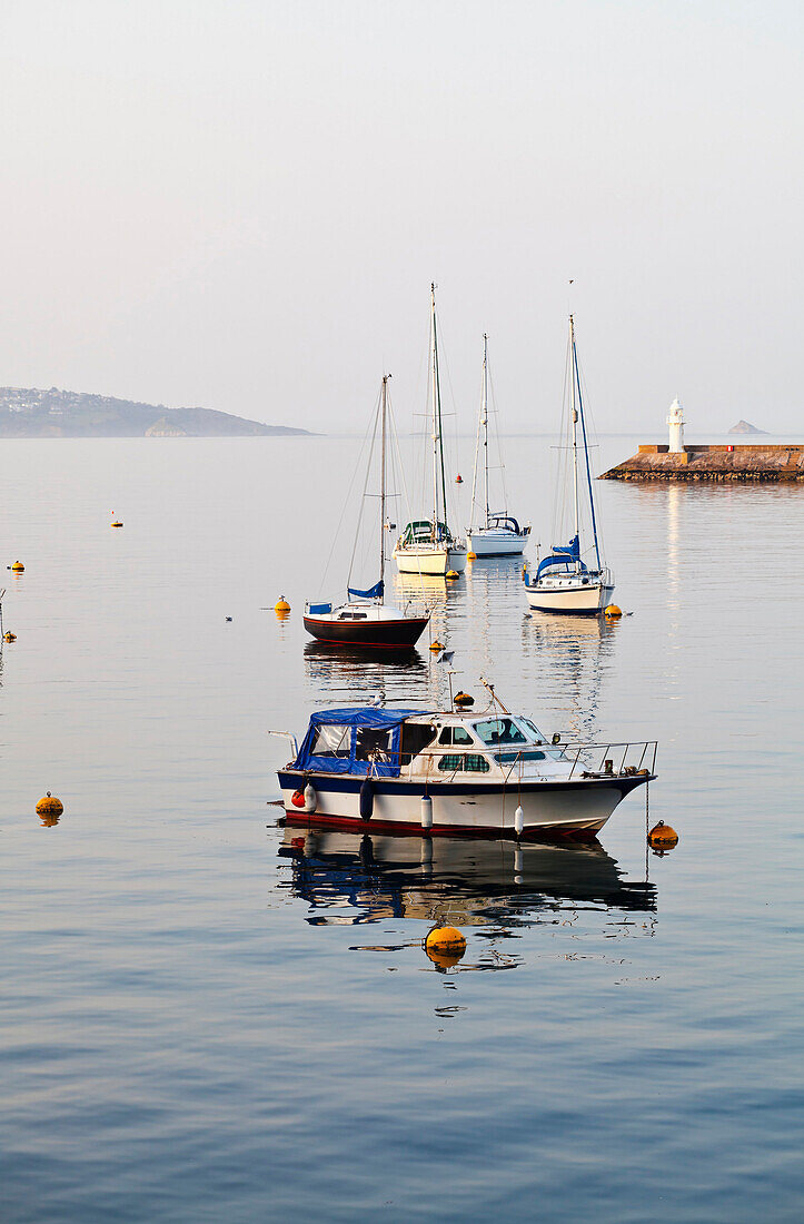 View out to sea on the English coastline, with  flat calm water. Sea wall, Sheltered mooring. Yachts and motor boats at anchor. Headland., Boats in a sheltered harbour