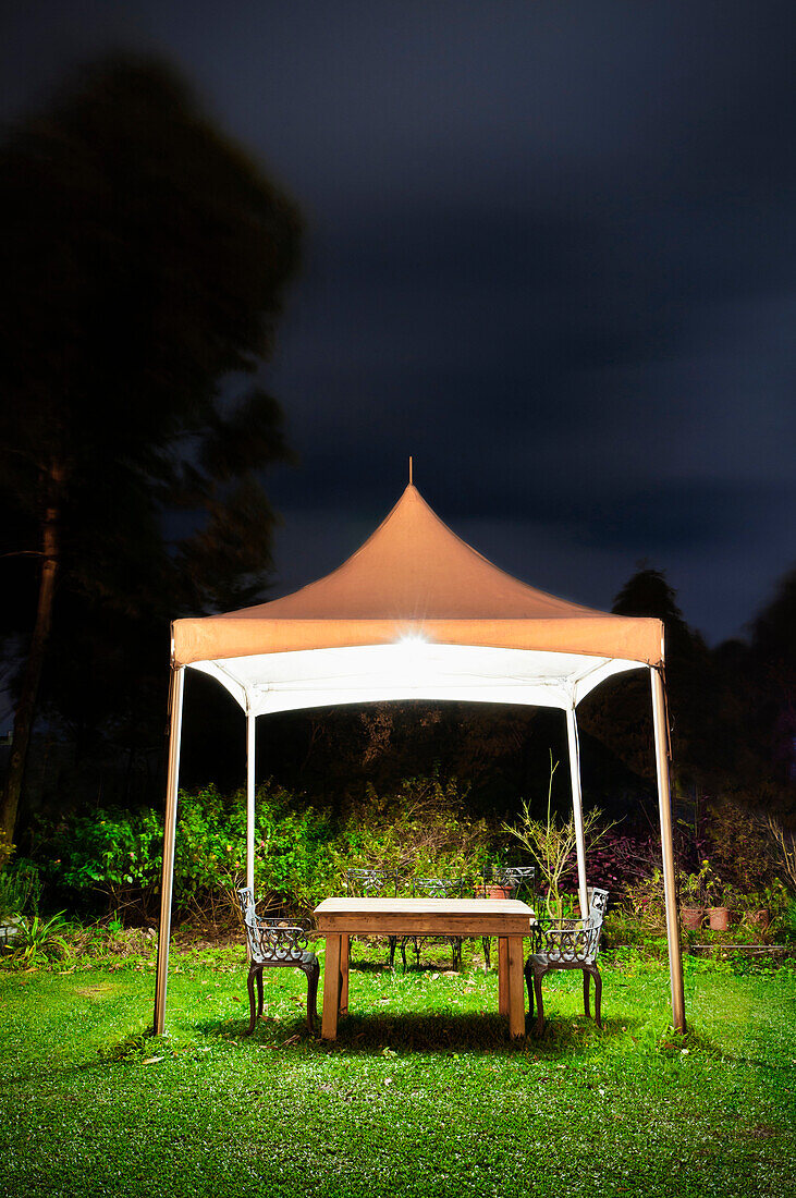 A small gazebo in a garden. Tent shape covering, over a table and seta. Space for working at night in the garden. Darkness. Silhouette of trees. Shrubs., Taoyuan county, Taiwan, Asia.