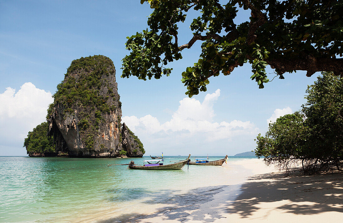 Long tail traditional boats beached and moored on Tham Phra Nang beach. Tall pillar or limestone karst rising from the sea water., Rai Leh, Krabi Province, Thailand