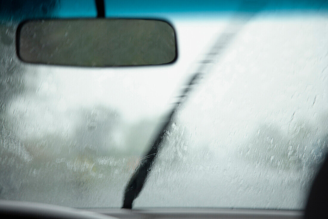 A view from inside a car, of the monsoon rain falling on the windshield of the vehicle. A windscreen wiper blade moving. A downpoor., Kep, Cambodia. A tropical storm.