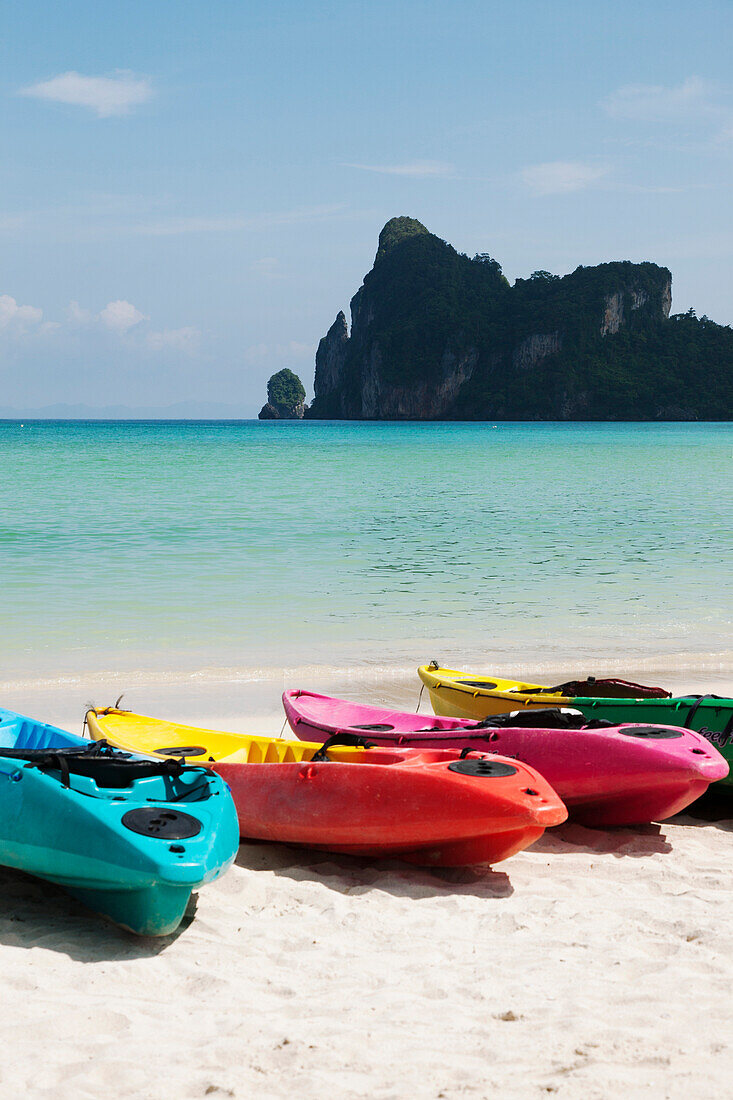 A tourist destination and resort in the Andaman islands off the cost of Thailand. A view out to sea from the white sand beach. Kayaks for hire on the beach. Rocky headland, and limestone karsts rising from the water., Ko Phi Phi Island, Krabi Province, Th