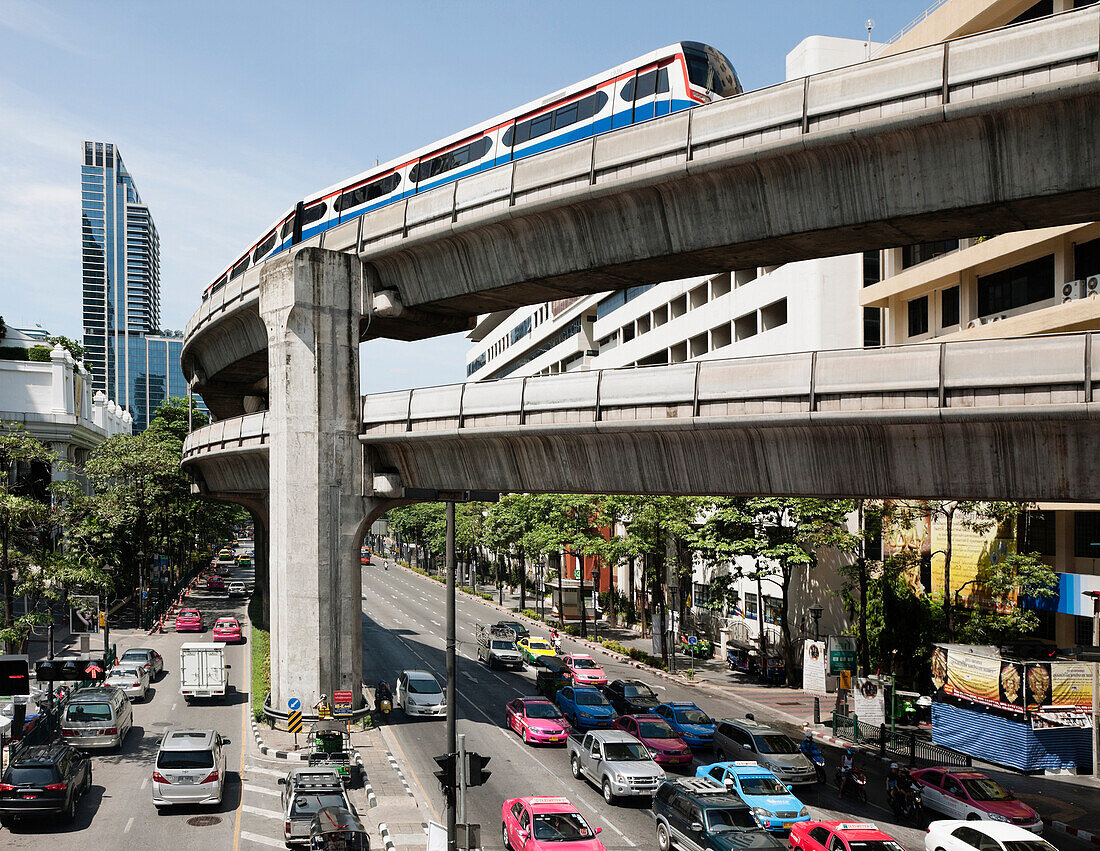 A mass transit train travelling on an elevated track above the city road. Traffic. Cars and buses on the multilane highway below. Urban scene., Bangkok, Thailand. Traffic and transport.