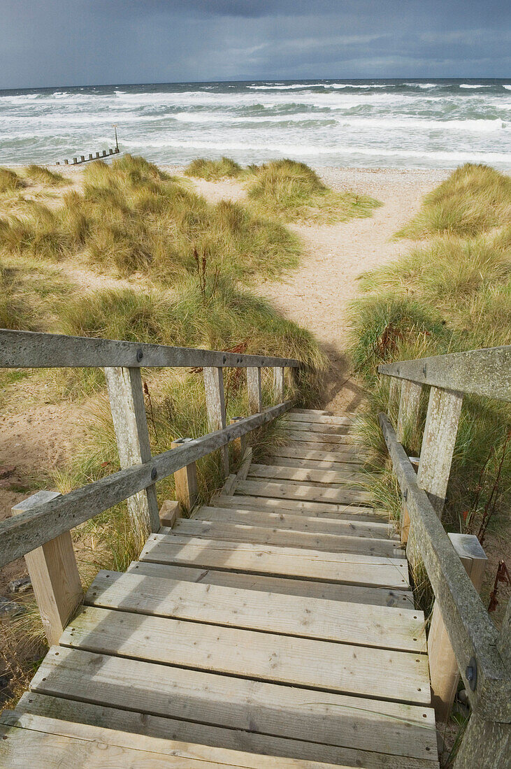 Wooden steps leading down through the dunes onto the shingle beach in winter, with a stormy sea in the background. Findhorn, Moray, Scotland., Steps down onto the beach, Findhorn, Scotland.