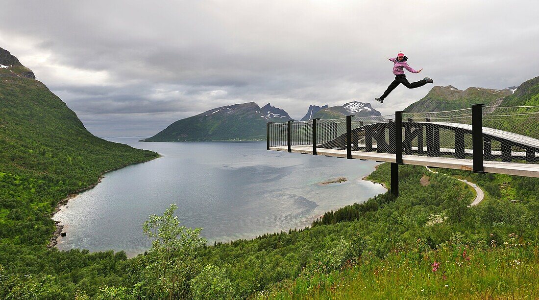 Junge Frau, die über den Fjord Bergsfjorden springt Landschaftsgestaltung der Nationalen Touristenroute Die Westküste der Insel Senja wurde als eine der spektakulärsten Landschaften Norwegens ausgewählt Insel Senja Grafschaft Troms, Norwegen, Nordeuropa