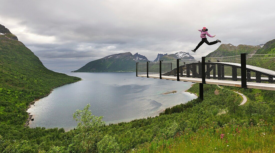 young woman jumping over the fjord Bergsfjorden Landscaping of the National Tourist Route The west coast of the island Senja has been selected as one of the most spectacular landscapes in Norway Senja island County of Troms, Norway, Northern Europe