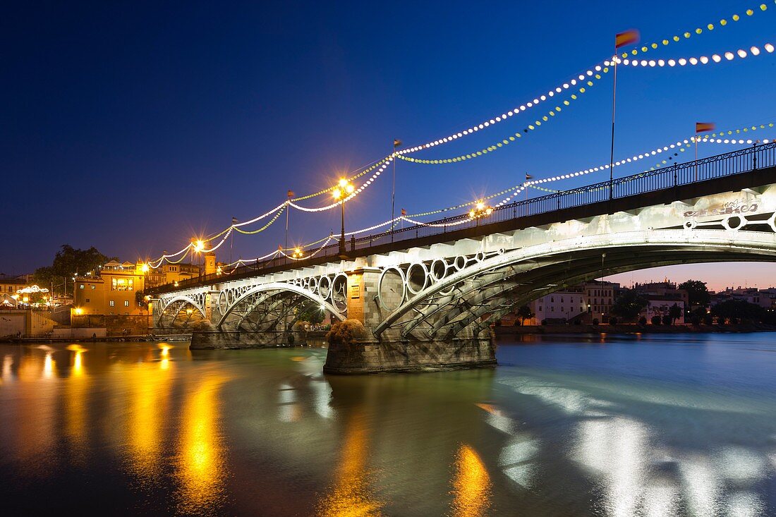 Triana bridge at dusk with decorative lighting for La Vela festival, Seville, Spain