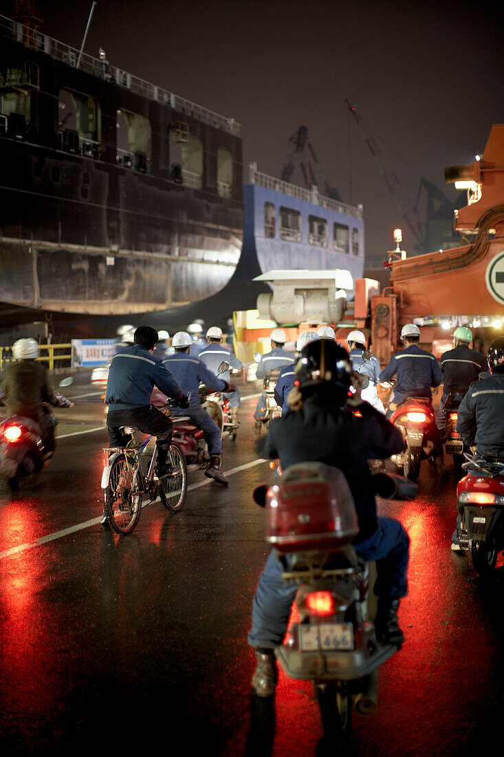 Workers on mopeds during shift change at night, Hyundai Heavy Industries (HHI) dockyard, Ulsan, South Korea