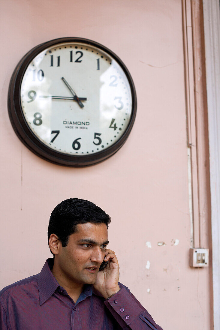 Indian talking on a mobile phone underneath a wall clock, Pune, Maharashtra, India