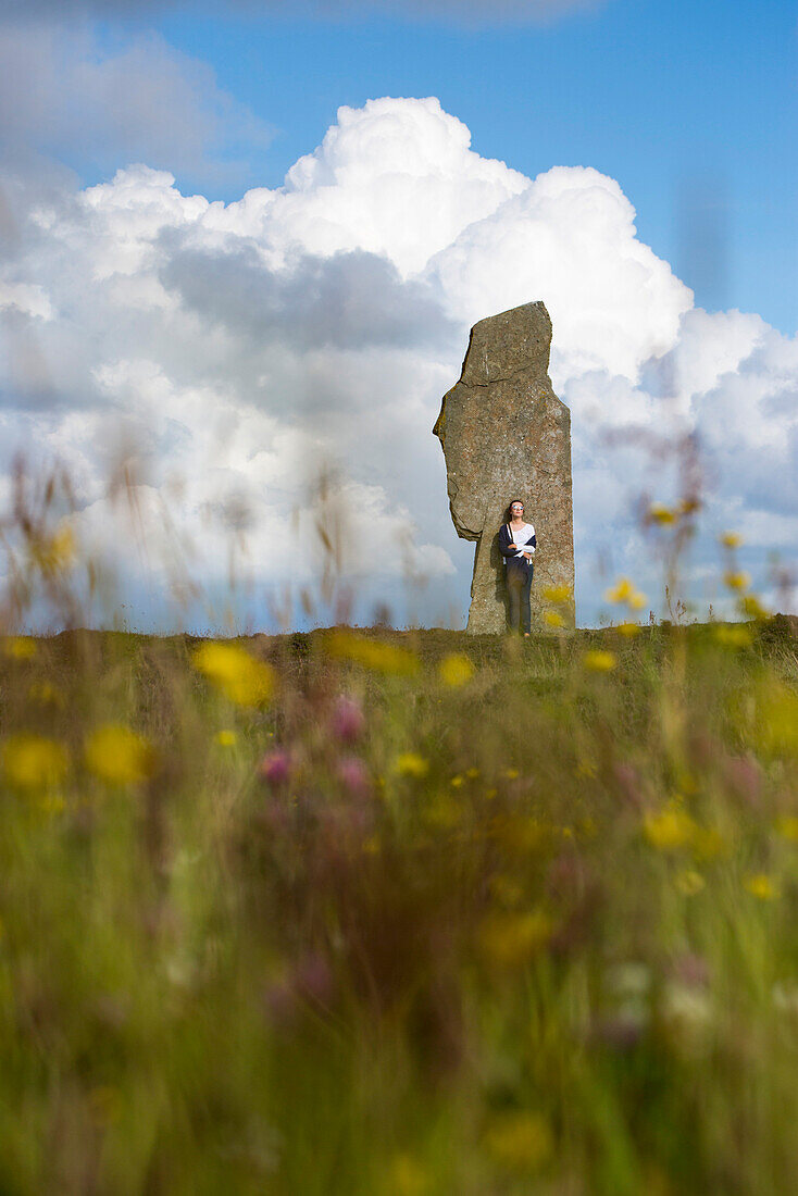 Young woman stands by stone at The Ring of Brodgar circle of Neolithic standing stones, Orkney Islands, Scotland, United Kingdom