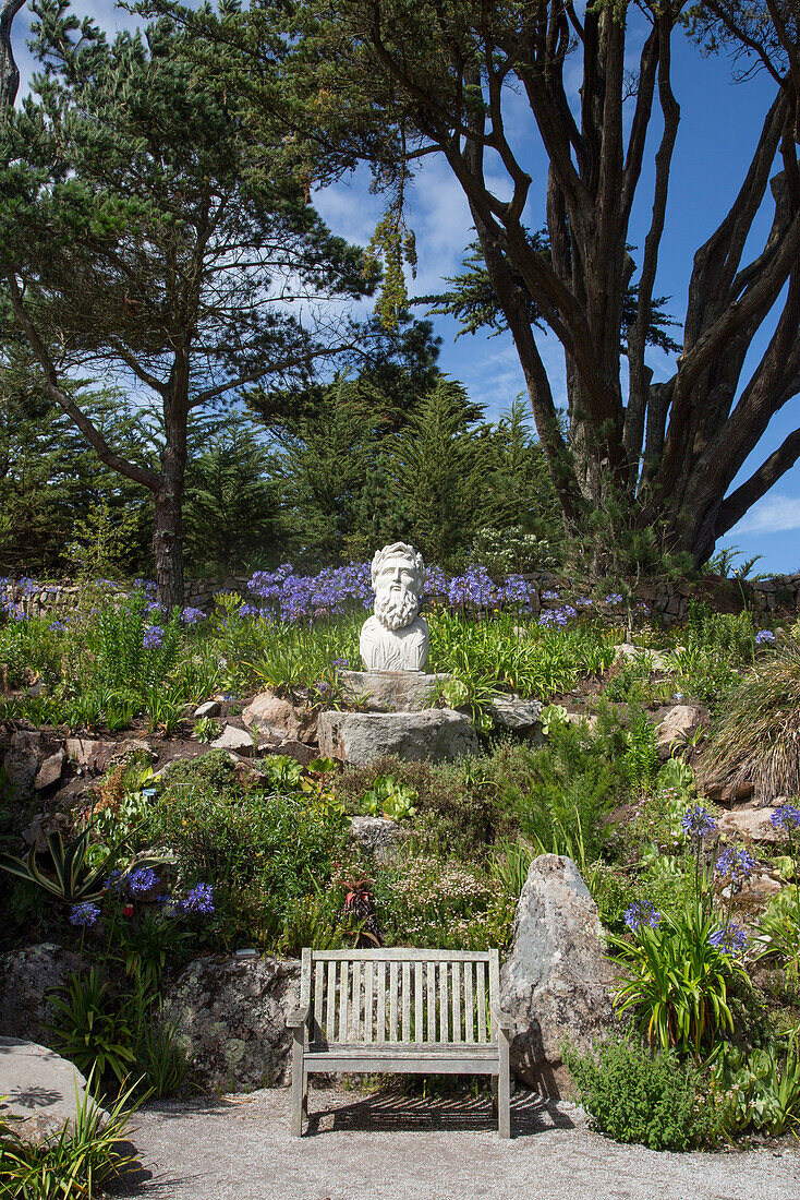 Eine Bank und eine Skulptur in den Gärten von Abbey Gardens, Tresco, Scilly-Inseln, Cornwall, England