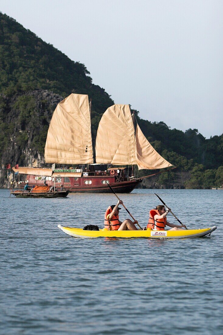 Kayakers paddle near a cruising junk Halong Bay Vietnam