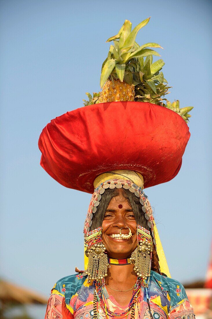 Asia,India,Goa,smiling woman carrying pineapple in basket on head on the beach
