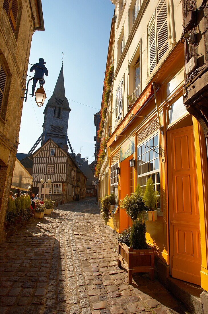 Narrow street with colourful shops looking towards the Bell tower of the Wooden Church of St Terezza - Market Square Honfleur Normandy France
