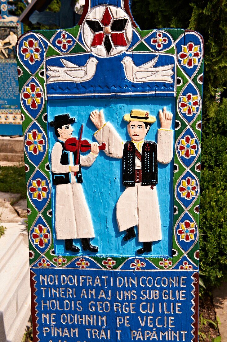 Tombstone showing a fiddler and a man doing a traditional dance, The Merry Cemetery  Cimitirul Vesel, Sapânta, Maramares, Northern Transylvania, Romania. The naive folk art style of the tombstones created by woodcarver Stan Ioan Patras 1909 - 1977