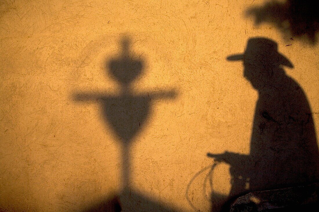 The shadow of a man wearing a hat and cycling is cast with a cross in a wall in San Gregorio Atlapulco cemetery, Xochimilco, Mexico City. The Day of the Dead celebration is a tradition that honors the deceased