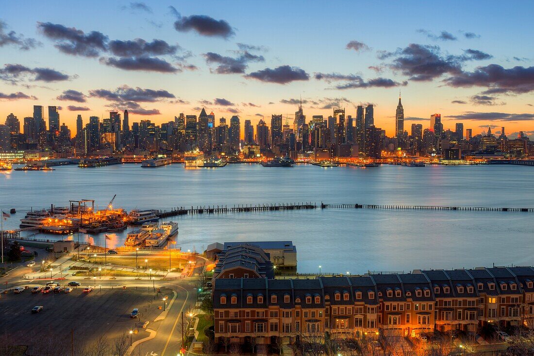 The Manhattan skyline in New York City during morning twilight as viewed over the Hudson River looking east from Weehawken, New Jersey. The eastern sky and clouds were accented with tinges of orange that began to show in the hour before sunrise.