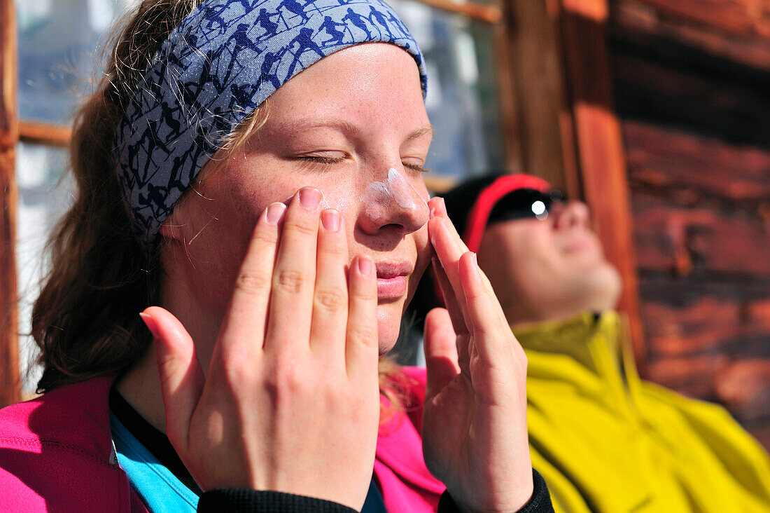 Junge Frau vor einer Almhütte cremt sich mit Sonnencreme ein, Kreuzspitze, Osttirol, Tirol, Österreich