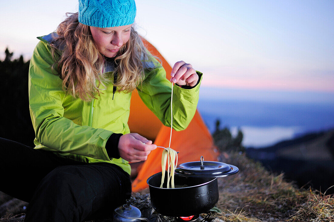 Junge Frau kocht Nudeln vor einem Zelt, Risserkogel, Bayerischen Voralpen, Mangfallgebirge, Bayern, Deutschland