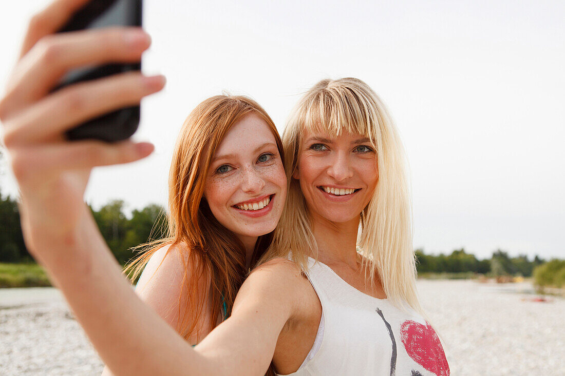 Two young women taking pictures of themselves by a mobile phone, Munich, Bavaria, Germany