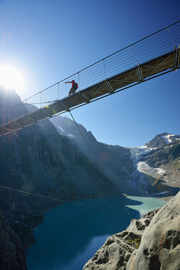 Hiker walking across a suspension bridge over a mountain lake, Trift glacier in the background, Trift glacier suspension bridge, Tieralplistock, Urner Alps, Bernese Oberland, Bern, Switzerland