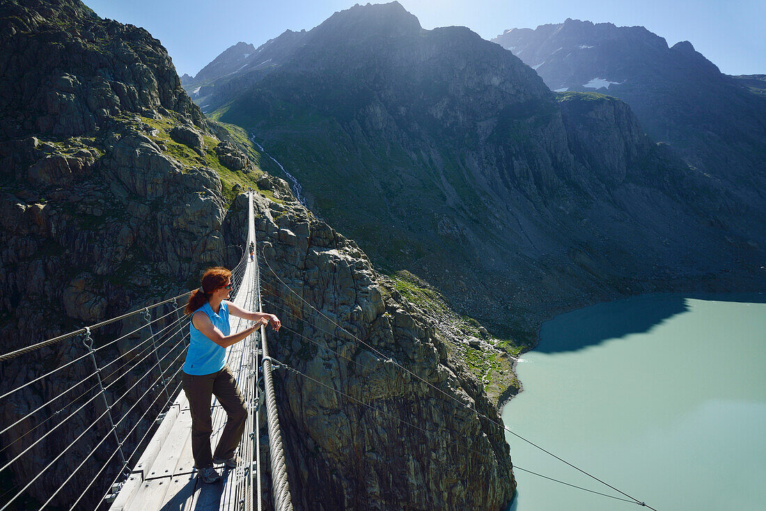 Woman standing on a suspension bridge over a mountain lake, Trift suspension bridge, Trift glacier, Tieralplistock, Urner Alps, Bernese Oberland, Bern, Switzerland