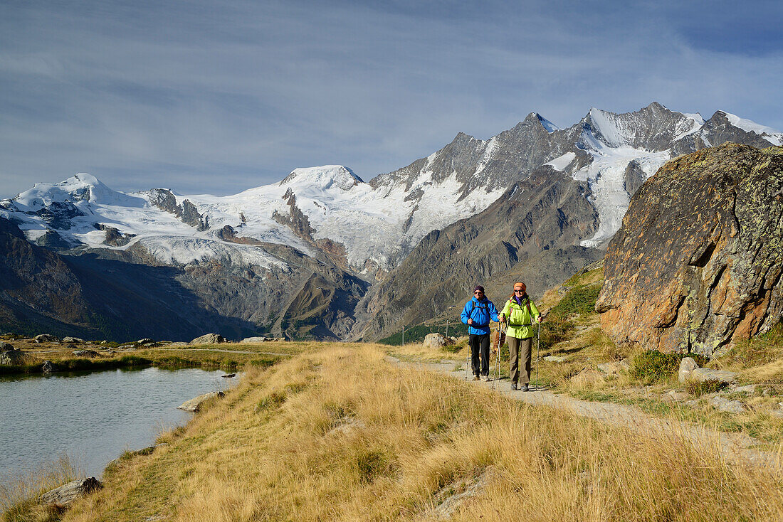 Woman and man hiking near a mountain lake with view to Mischabel range with Allalinhorn, Alphubel, Täschhorn, Dom and Lenzspitze, Pennine Alps, Valais, Switzerland
