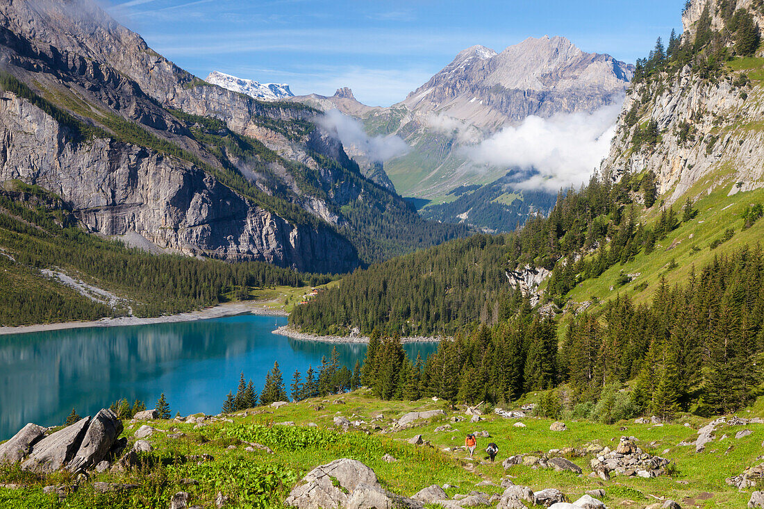 A man and a woman hiking above lake Oeschinen, Alp Unterbärgli, view to Wildstrubel, Bernese Oberland, Canton of Bern, Switzerland