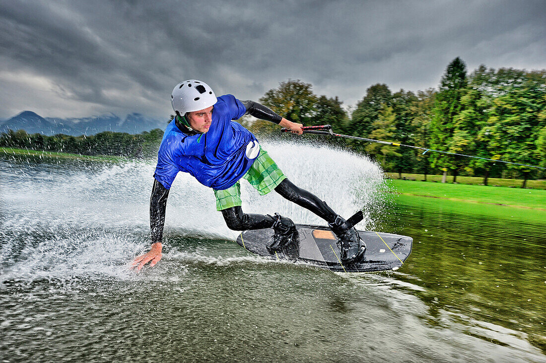 Young man surfing on a wakeboard, wakeboarding at lake Neubeurer See, Neubeuern, Rosenheim, Upper Bavaria, Bavaria, Germany