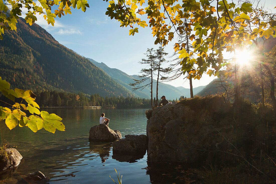 Frau und Mann sitzen auf Felsblöcken am Ufer des Hintersees, Ramsau, Berchtesgadener Land, Nationalpark Berchtesgaden, Oberbayern, Bayern, Deutschland, Europa