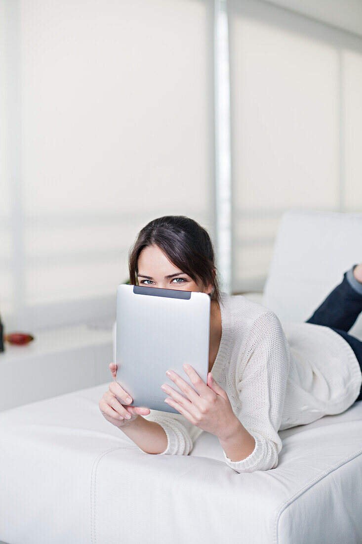 Playful brunette woman on a couch with tablet smiling at camera