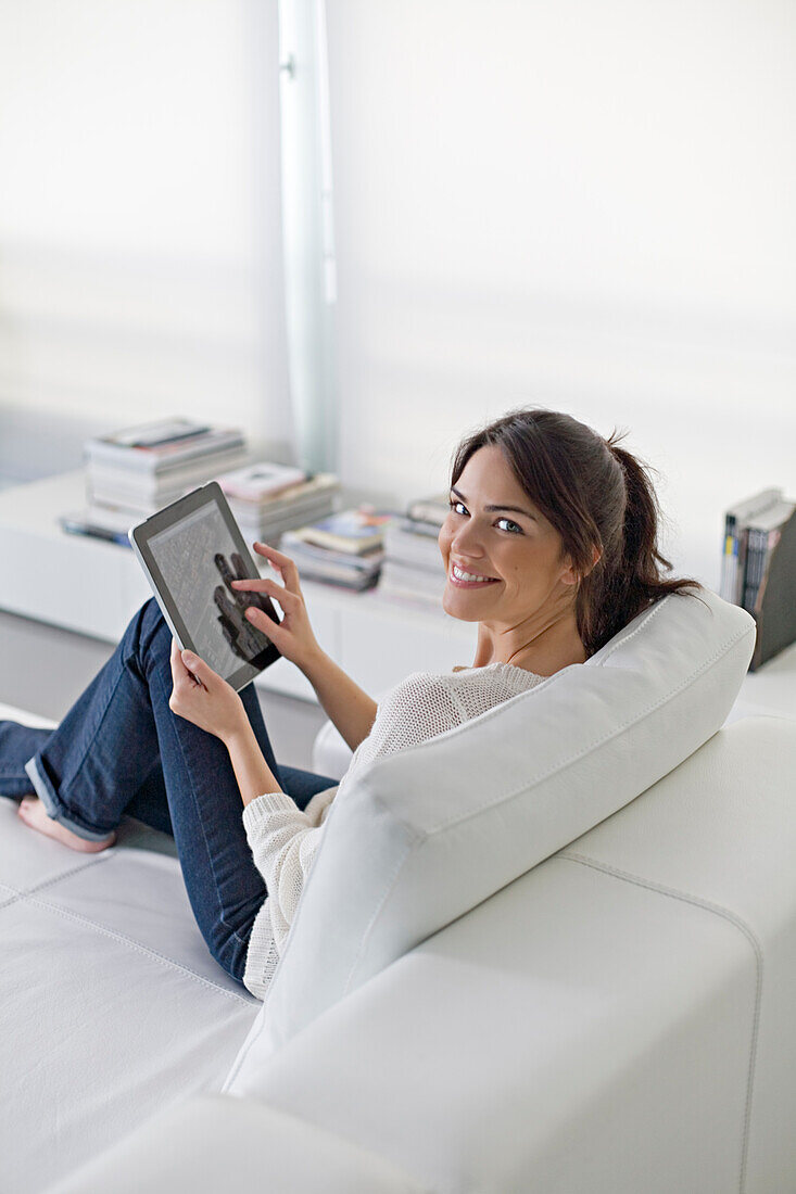 Beautiful brunette woman on a couch with tablet smiling at camera