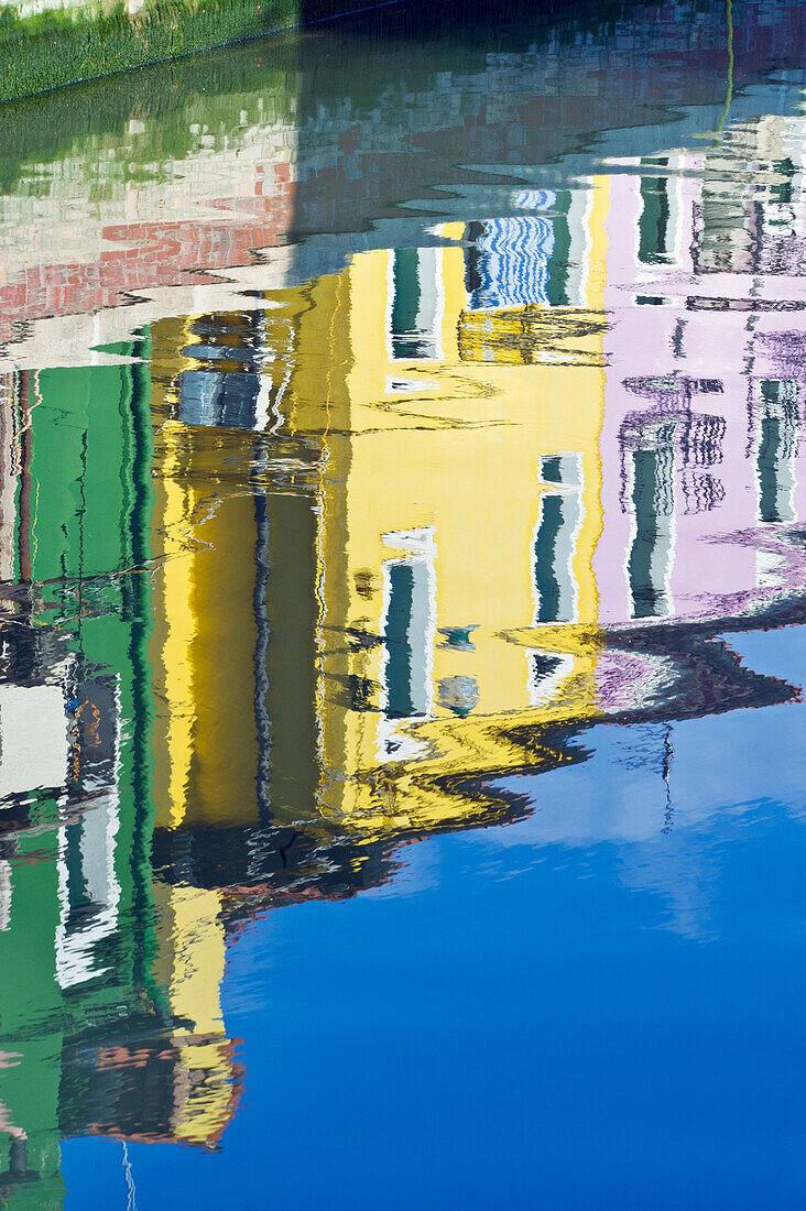 Historic houses painted in different colours, reflected in the water of the canal.