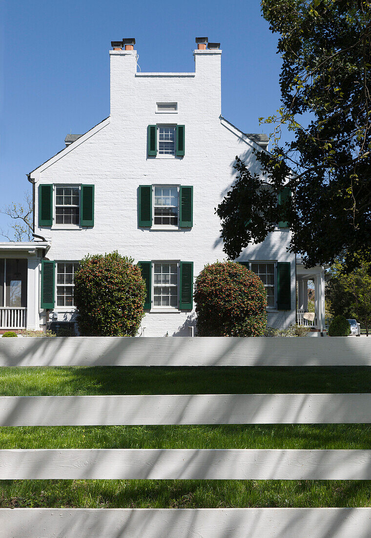 A plantation style home, in 18th century style, viewed over a wooden fence.