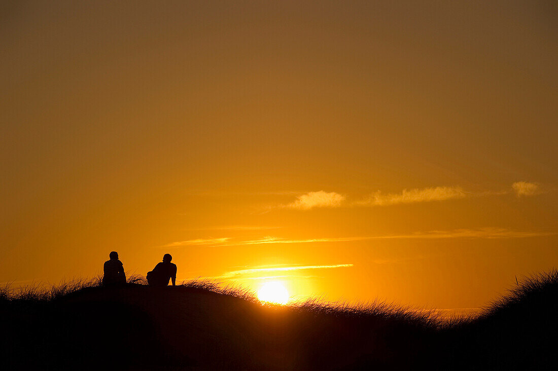 A couple sitting and watching the sunset, sandbank near Nebel, Amrum, North Frisian Islands, Schleswig-Holstein, Germany