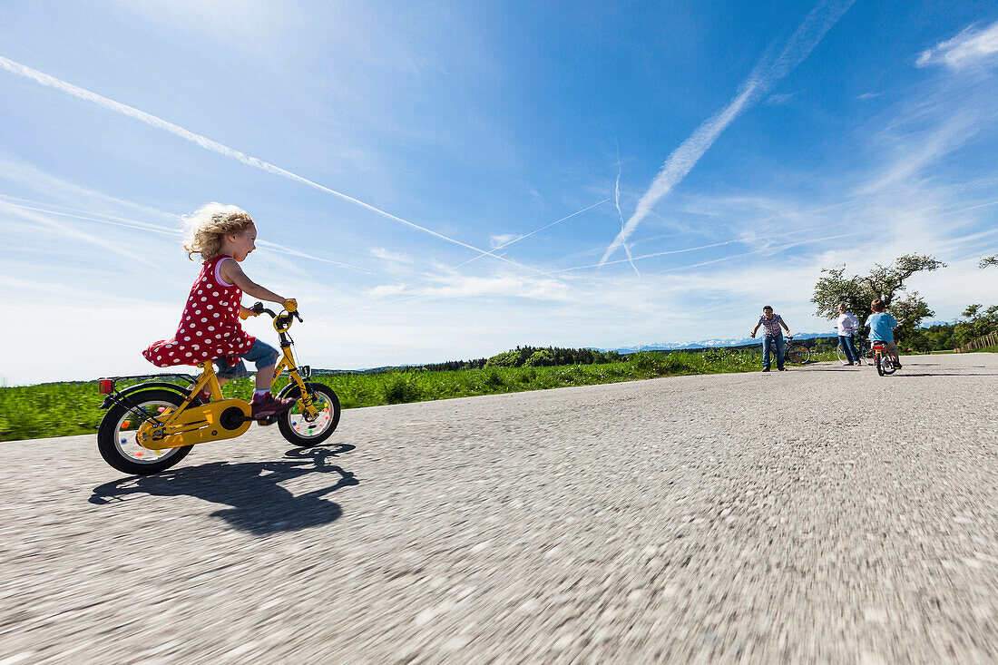 Kinder fahren Fahrrad, Eltern stehen im Hintergrund, Oberbayern, Bayern, Deutschland