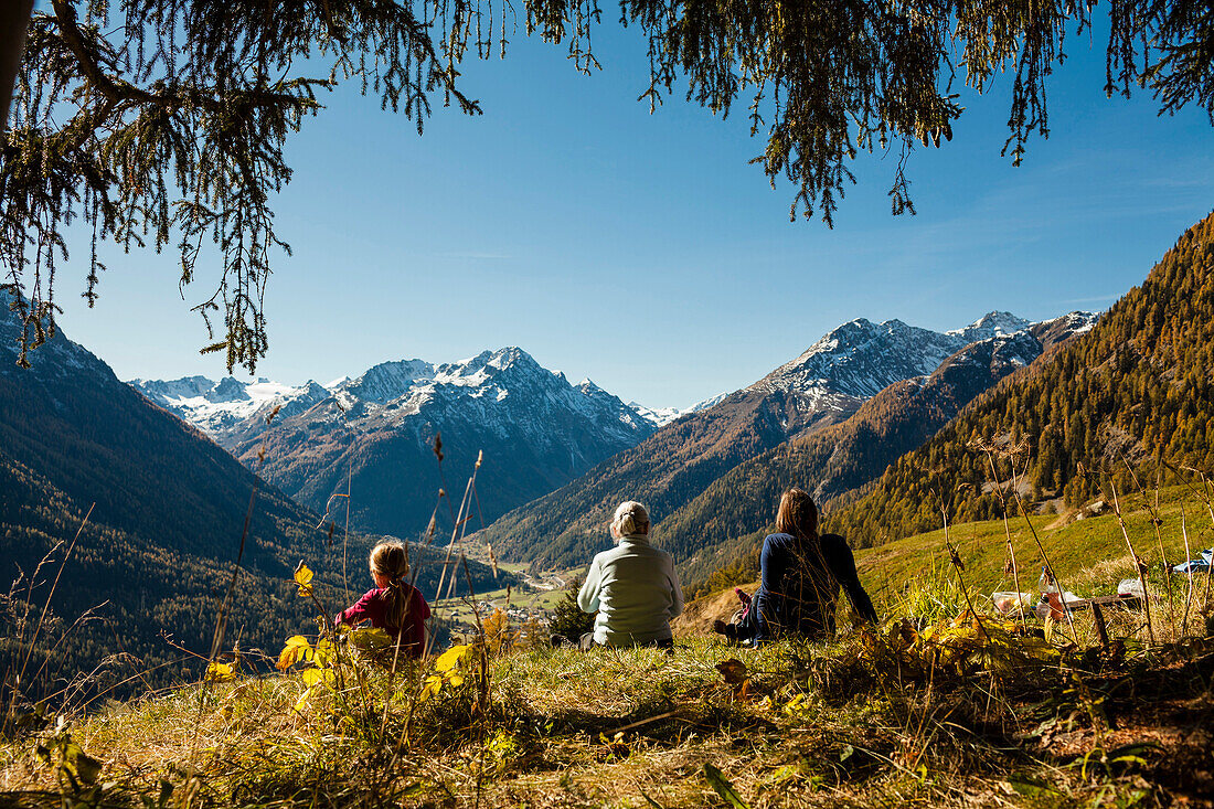 A family, two girls, a younger and an older woman sit on a meadow, autumn at Guarda, Engadin, Graubuenden, Grisons, Switzerland