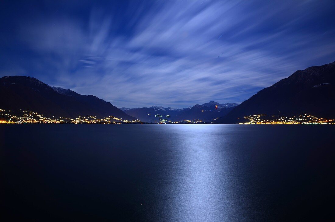 Reflected moon light over an alpine lake maggiore with snow-capped mountains and clouds in ticino switzerland
