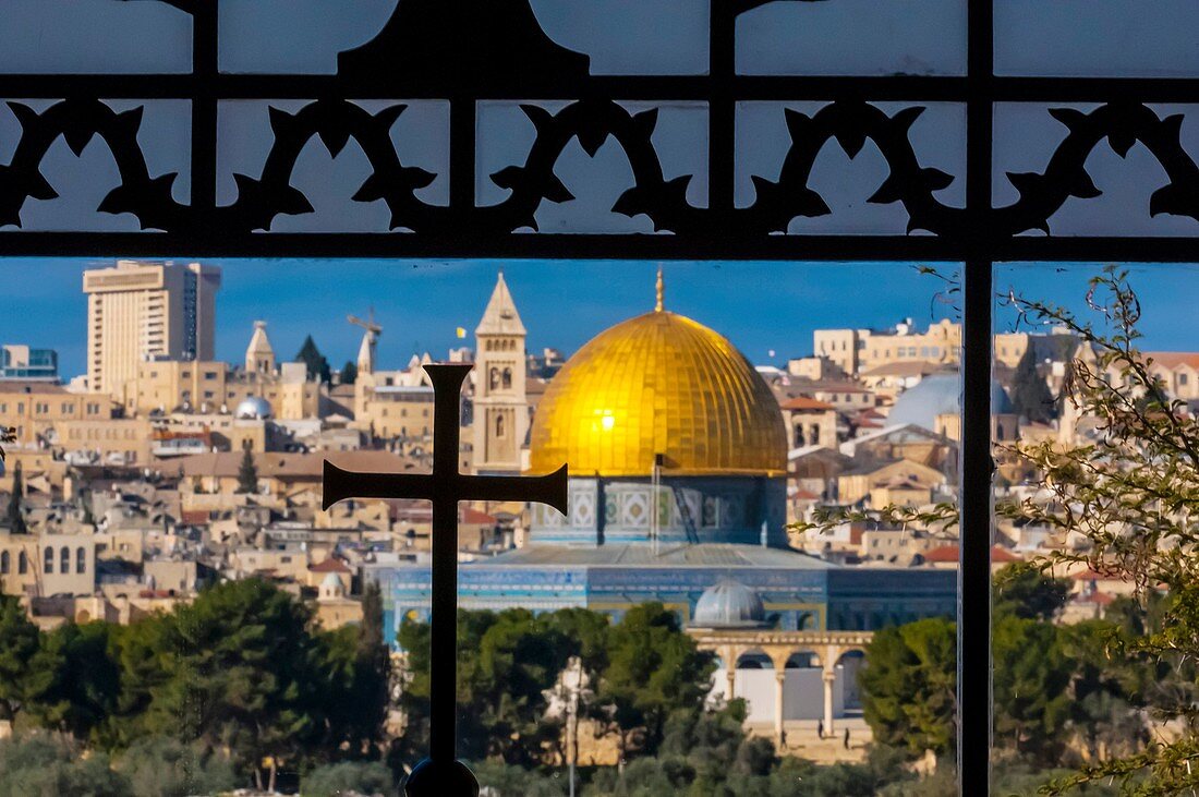 The Dome on the Rock on the Temple Mount, viewed through an ornate window with a cross in the Sanctuary of Dominus Flevit Roman Catholic church on the Mount of Olives, Jerusalem, Israel