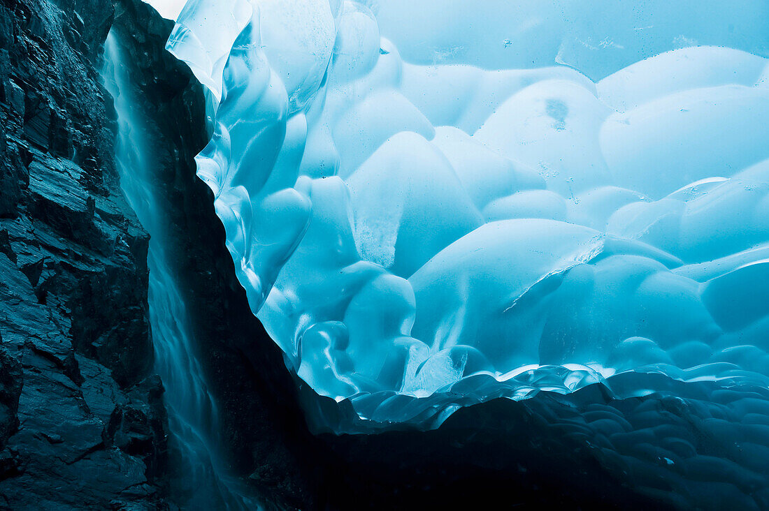 A waterfall trickles its way down the rock face of an ice cave inside the Mendenhall Glacier, Juneau, Southeast Alaska, Summer