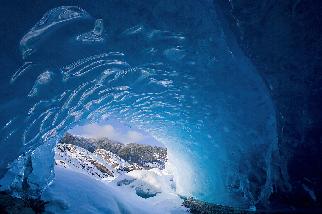 View from inside an ice cave looking outward at the snowcovered landscape, Mendenhall Glacier near Juneau in Southeast Alaska, Winter