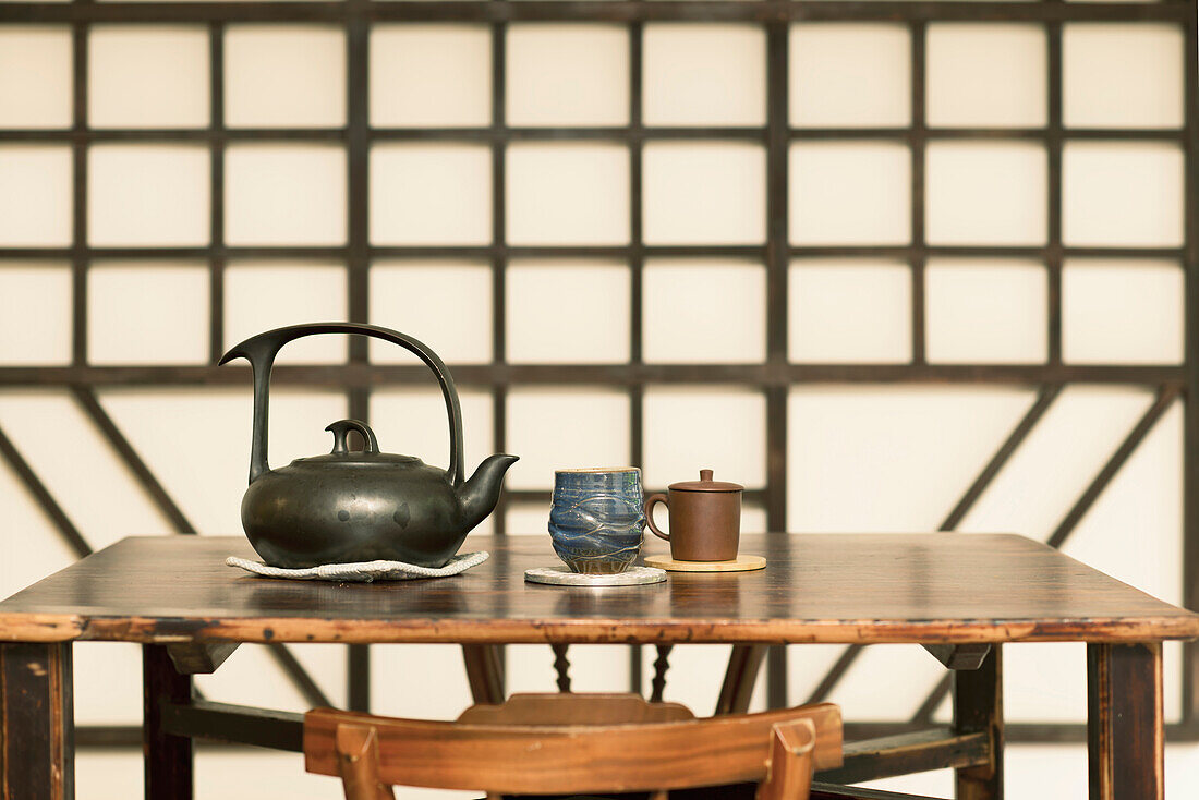 A Chinese style wooden table, with a pottery teapot and cups. A wooden geometric frame wall decoration. Living room in a house.