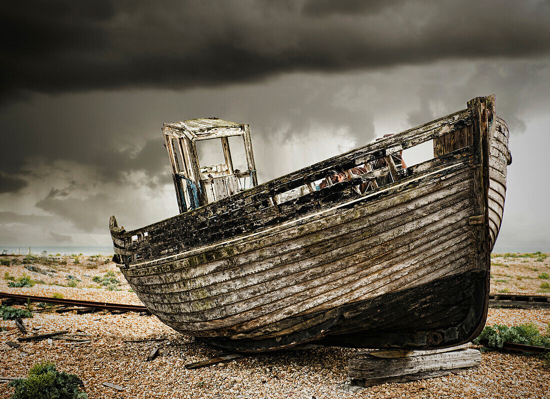 A wooden fishing boat, on the beach at Dungeness. A dark stormy sky.