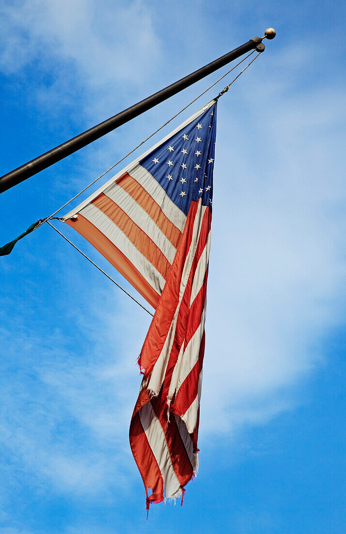 An old tattered frayed flag, the Stars and Stripes national American flag, flying on a flag pole.