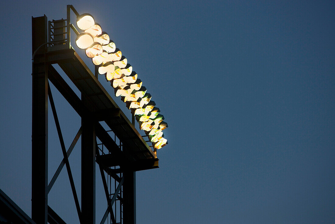 A tall lighting gantry or tower with strong powerful floodlights, over a sports area or stadium.