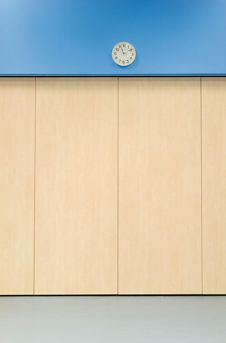 Clock on a blue wall in the main hall of a secondary school.