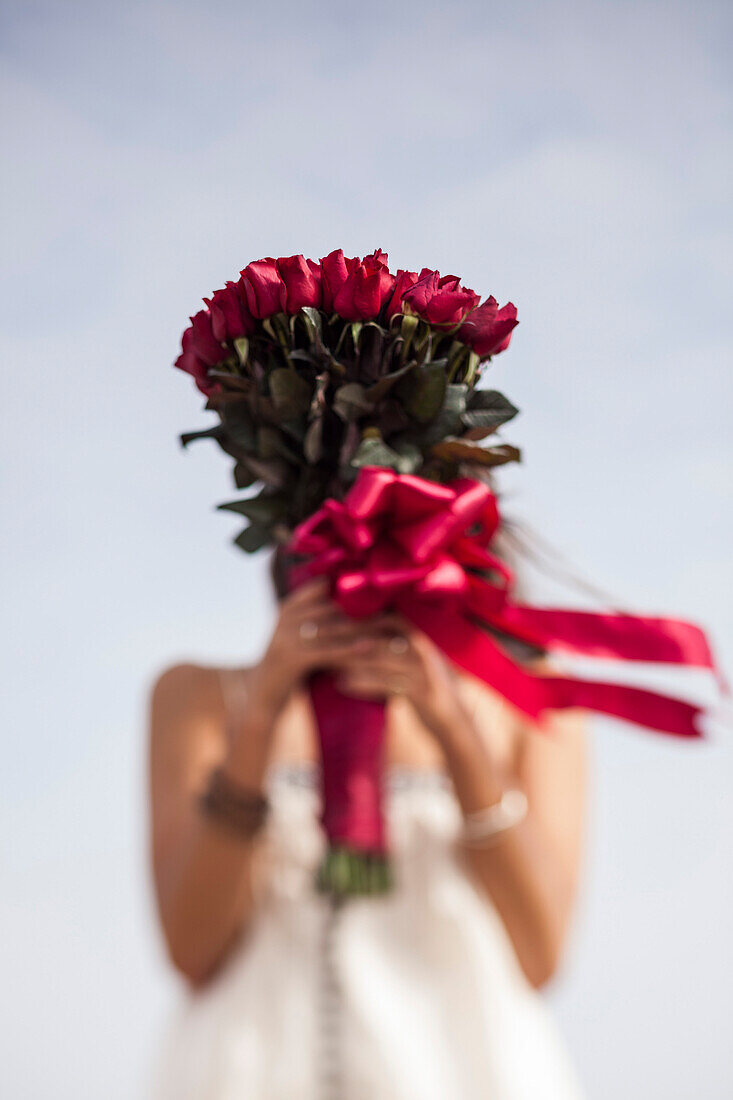 Young Woman Holding Bouquet of Red Roses in Front of Face