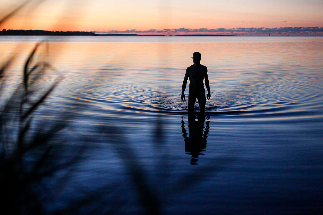 Mann steht im Wasser in der Dämmerung, Altefähr, Insel Rügen, Mecklenburg-Vorpommern, Deutschland