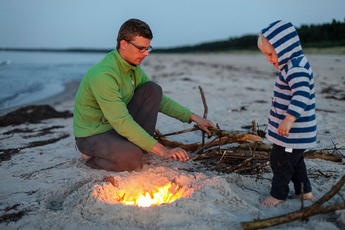 Vater und Sohn (2 Jahre) machen ein Feuer am Strand, Schaabe, Insel Rügen, Mecklenburg-Vorpommern, Deutschland